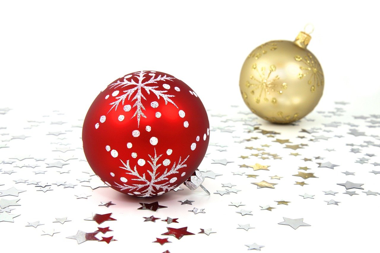 One red and one golden artistically designed Christmas bulb against a white background with silver stars beneath them